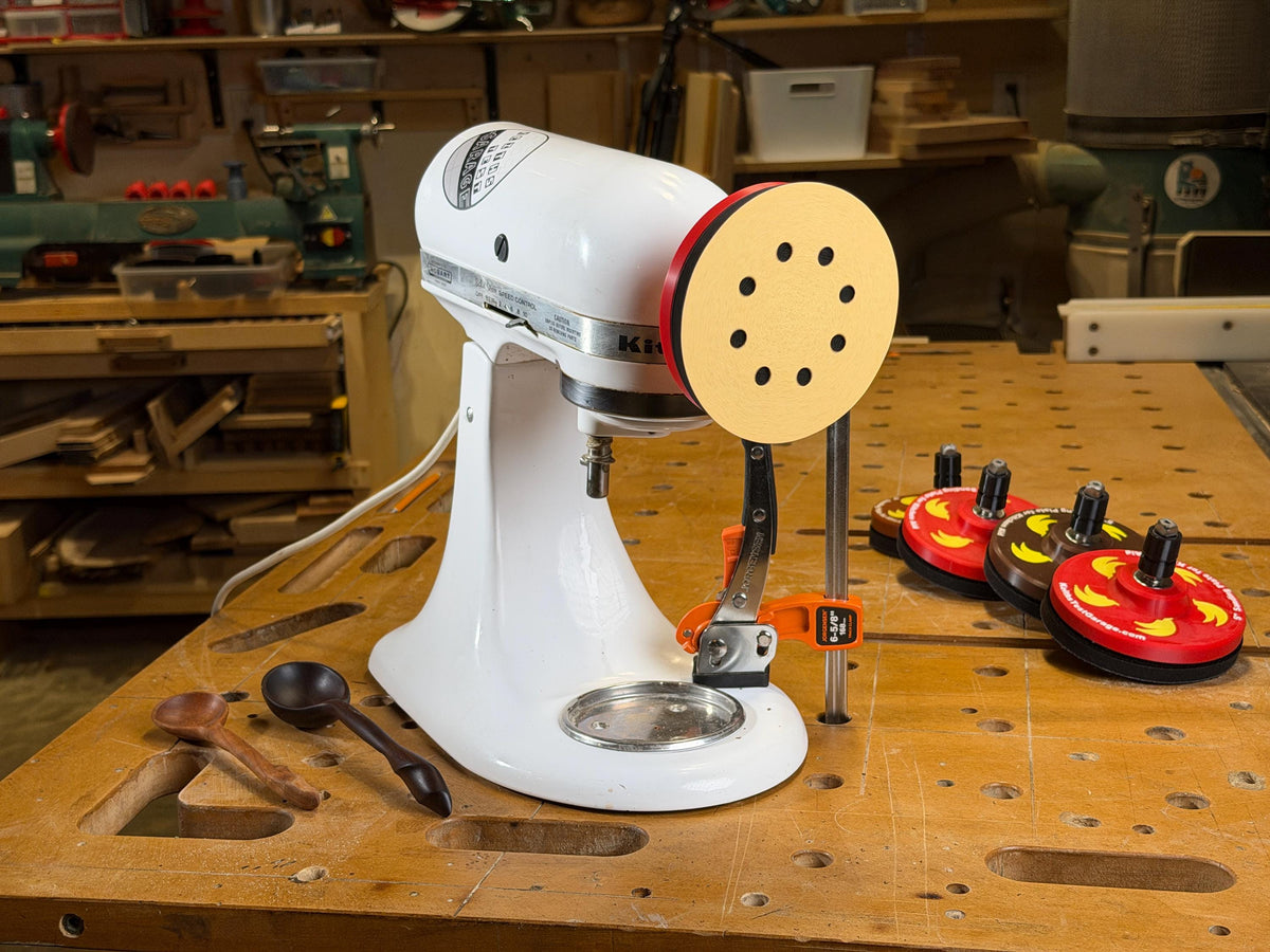 Disc sander attachment mounted on a KitchenAid stand mixer with carved wooden spoons